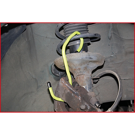 Nahaufnahme der Fahrzeugfederung. Gelbe Schlauchleitung gewickelt um Federbein. Rostige Metallteile dominieren.